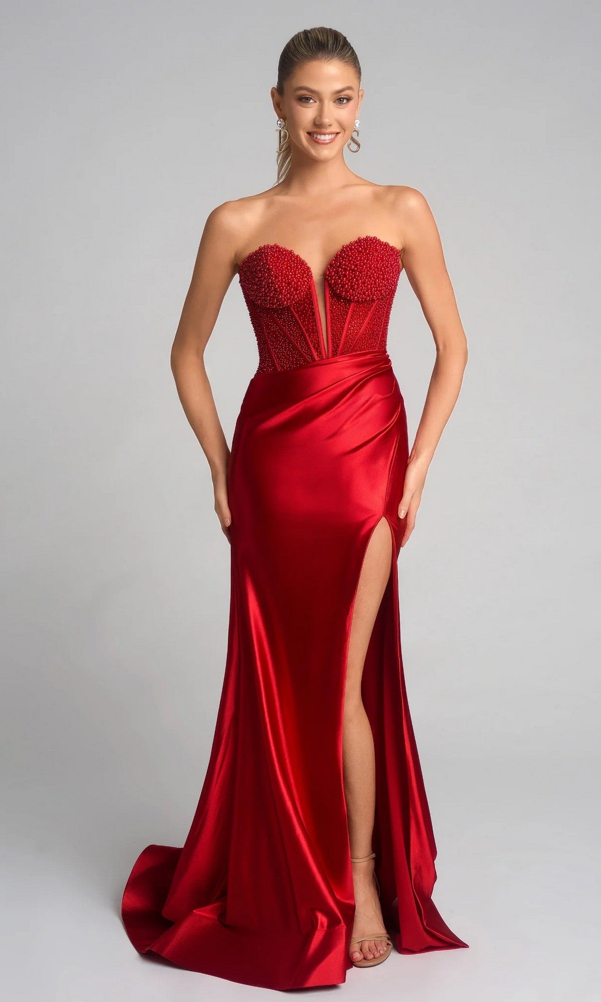Woman wearing the Portia and Scarlett PS26039 long prom dress with a beaded corset bodice, strapless fitted red silhouette, high slit, and silky skirt, posing against a plain light background.